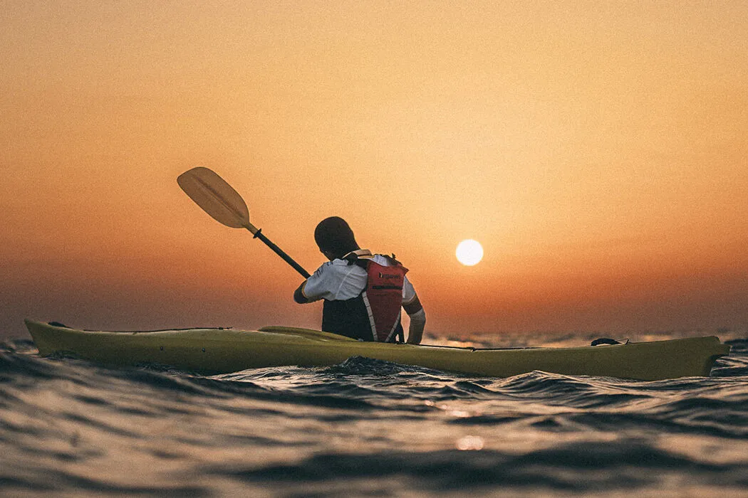A man in a canoe on the ocean at dusk